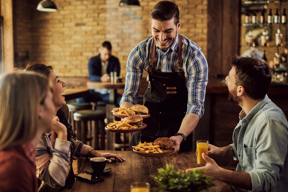 A friendly waiter serving burgers and fries to customers at a restaurant